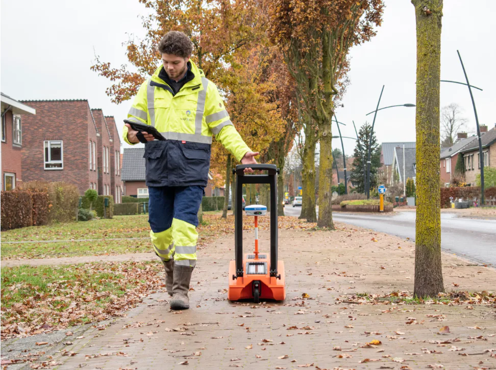 Bouwvakker loopt met grondradar door de straat terwijl hij op een iPad kijkt.